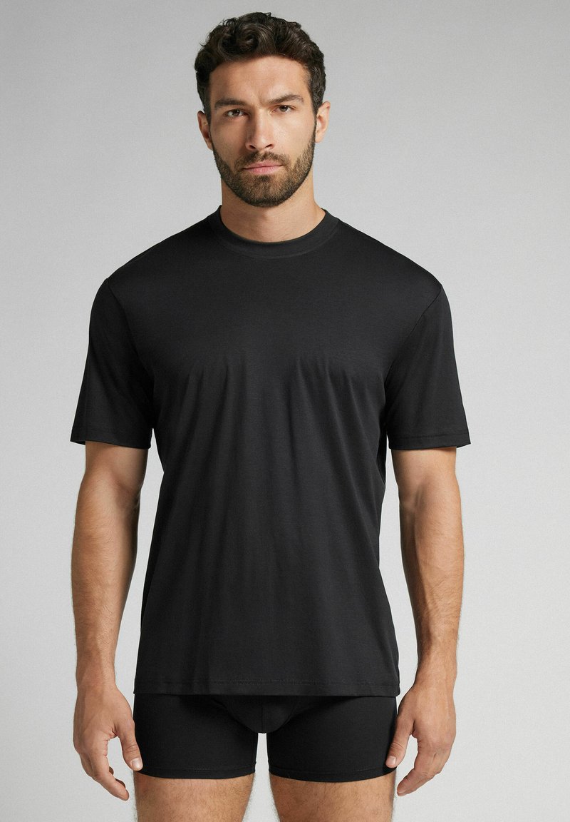 Černé tričko s krátkým rukávem vyrobené z hladké tkaniny, má kulatý výstřih a volný střih, doplněné o černé boxerky.