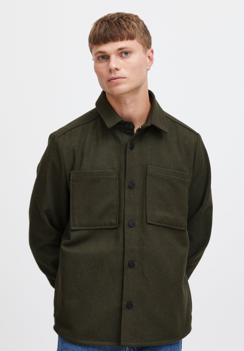 Camicia verde oliva con bottoni, realizzata in un tessuto testurizzato, dotata di colletto a punta, due tasche sul petto e bottoni neri, progettata con una vestibilità rilassata.