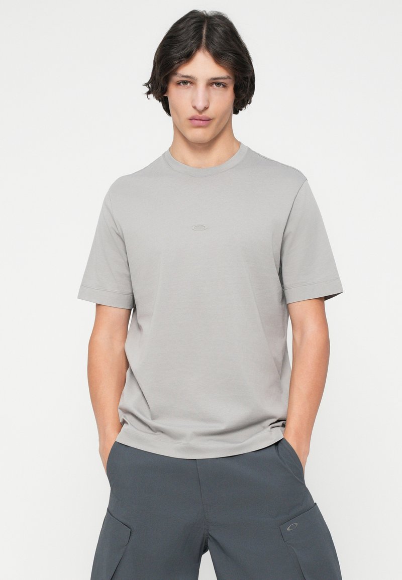 Graues T-Shirt mit kurzen Ärmeln und Rundhalsausschnitt. Hergestellt aus weichem Stoff, mit einem kleinen, dezenten Logo auf der Brust. Schlichtes Design, minimale Details.