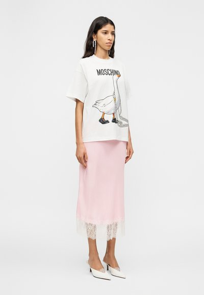 Λευκό T-shirt Moschino με κοντά μανίκια και γραφική στάμπα πάπιας, συνδυασμένο με ροζ σατέν φούστα με δαντελωτή διακόσμηση και λευκές μυτερές γόβες.