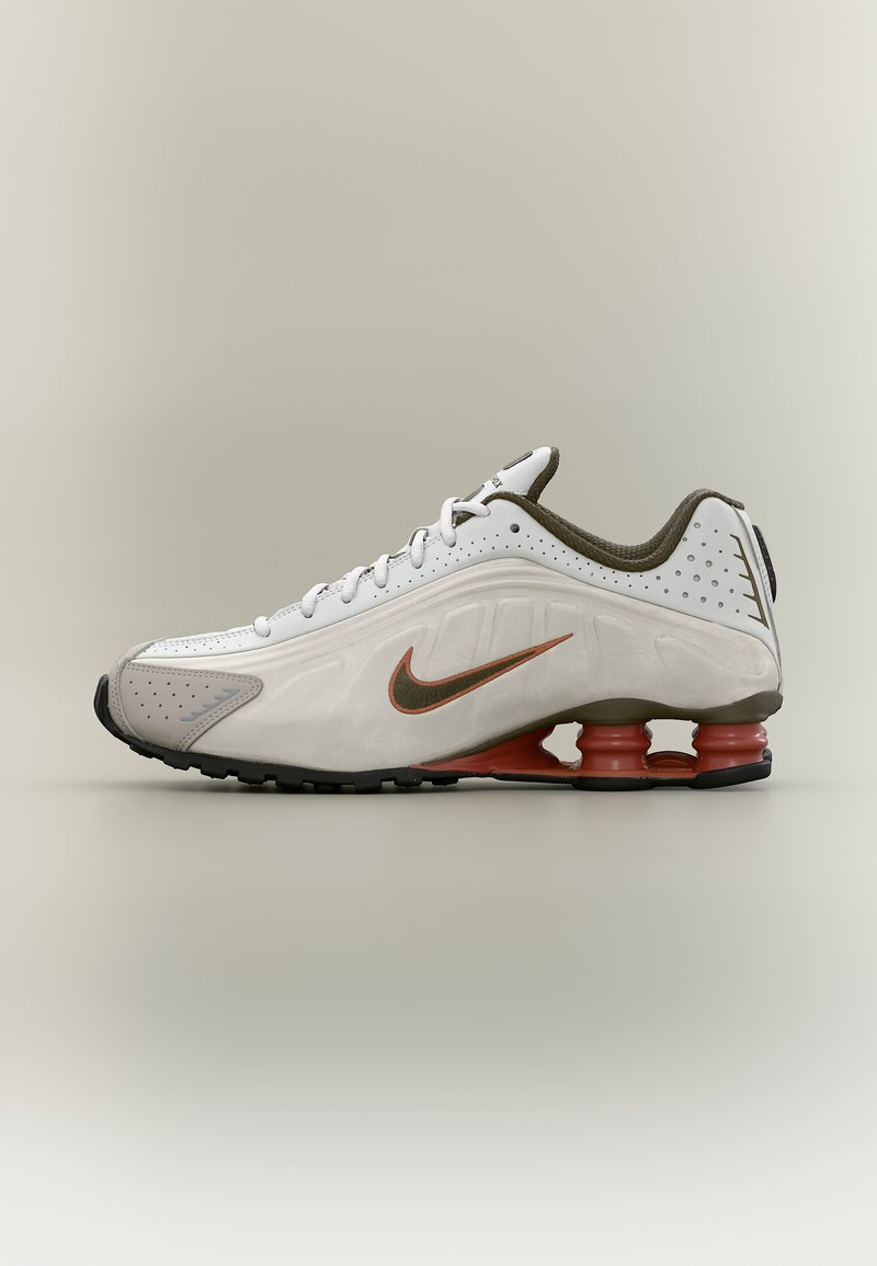 Άσπρο αθλητικό παπούτσι με πορτοκαλί σημάδι Nike, σόλα με ελαστική απορρόφηση κραδασμών, μαύρη σόλα και καφέ εσωτερική επένδυση, εμφανιζόμενο σε πλευρικό προφίλ.