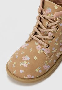 Bottines à fleurs marron avec des accents roses, dotées d'un dessus texturé, d'œillets dorés et de lacets tressés. Petit motif de fleurs multicolores.
