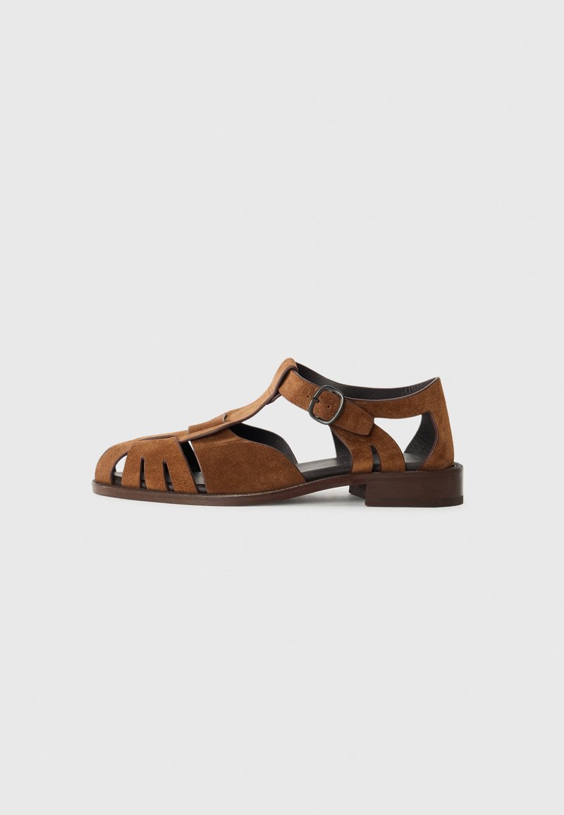 Brown suede sandals featuring cut-out designs, a round toe, a low heel, and an adjustable buckle strap for secure fit.