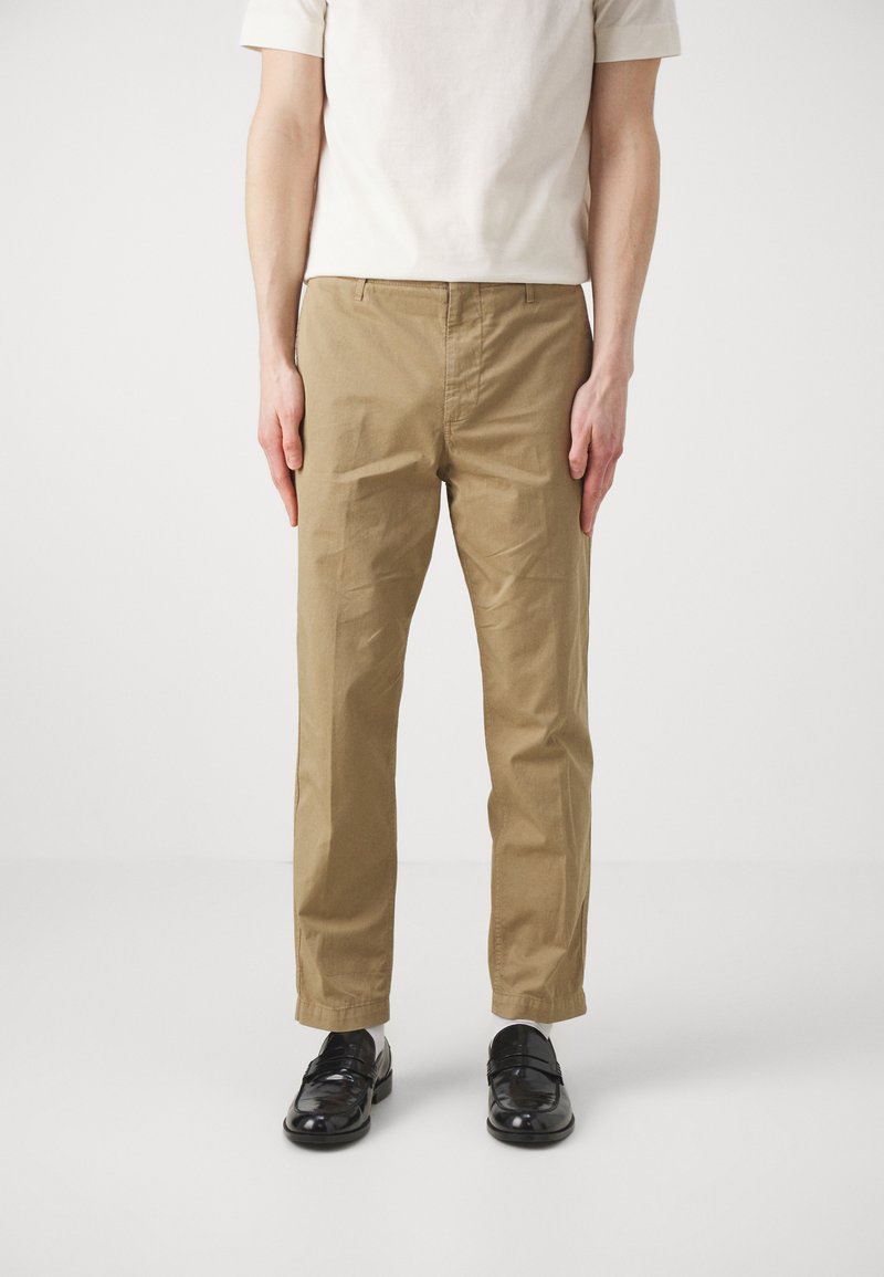 Pantalons en coton kaki au style droit, tissu léger, poches latérales et finition lisse, associés à des chaussures noires.