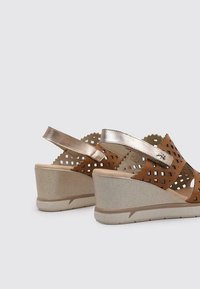 Sandalias de cuña marrones con diseño recortado, con una correa de acento metálico y suela texturizada. Presentan un tacón de cuña sólido en color beige claro.