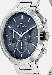 Montre en acier inoxydable argenté avec un cadran texturé bleu, trois sous-cadrans, index horaires blancs et accent de logo. Elle est dotée d'un bracelet poli.