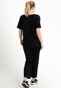 Black t-shirt with short sleeves, relaxed fit, and a rounded hem, paired with black pants and black athletic shoes. Simple and sleek design.