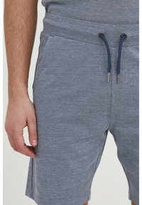 Grijze textuur shorts met een trekkoord in de taille, zijzakken en een relaxte fit. De stof lijkt zacht en lichtgewicht.