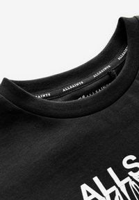 Must t-särk, millel valge "ALLSAINTS" trükk kaeluse sees ning osaliselt nähtav valge tekst ees.