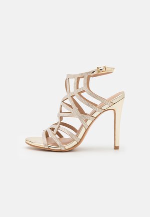Guld højhælet sandal med flere tynde remme dekoreret med små rhinsten og lukning med ankelspænde.