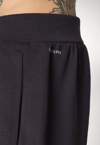 Shorts en tissu noir avec une taille élastique douce et un discret détail de pli. Présente un petit logo blanc avec l'inscription "CUDSPUN."
