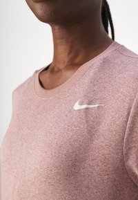 Roosa lühikese varrukaga T-särk struktuurses kangas, millel on vasakul rinnal valge Nike logo. Ümar kaelus ja mugav istuvus.