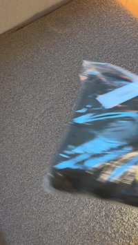 Emballage en plastique noir avec une surface brillante. Accents bleus et jaunes visibles, avec des détails de couture le long des bords et une section avant transparente.