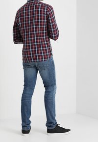 Checkered flannel shirt in burgundy, blue, and white, paired with blue denim jeans and black sneakers, viewed from the back.