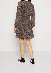 Schwarzes Blumenkleid mit langen Ärmeln, durchscheinendem Stoff, gerafftem Taillenbund und Rüschensaum, kombiniert mit schwarzen High-Top-Sneakers.
