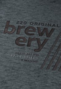 Mörkgrått textil med en texturerad yta, med präglad brun text "220 ORIGINAL brewery" och randiga accenter.