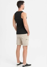 Zwarte mouwloze tanktop en beige shorts. De shorts hebben een ritszak. De outfit wordt gecompleteerd met zwart-witte sneakers.
