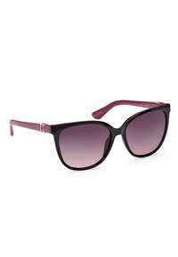 Lunettes de soleil en plastique noir en forme d'œil de chat avec des verres dégradés violets et des branches prune foncé, présentant un accent doré en forme de G sur la branche.