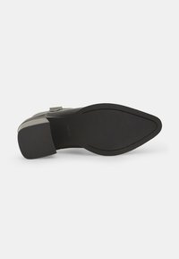 Zapato de cuero negro con puntera puntiaguda y suela de goma texturizada. Presenta un tacón bajo y cuadrado con un diseño minimalista.