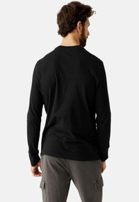 Zwarte langearms T-shirt van katoen, met een ronde hals en een rechte zoom, gecombineerd met grijze cargobroek met zijzakken.