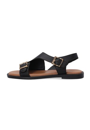 Schwarze Ledersandalen mit überkreuzten Riemen und goldenen Schnallenakzenten, mit einem braunen Fußbett und flacher schwarzer Außensohle.