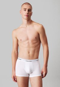 Hvide bomulds boxer briefs med en sort og hvid elastisk talje, der har "Calvin Klein" branding. Pasformen er tætsiddende og sømløs.