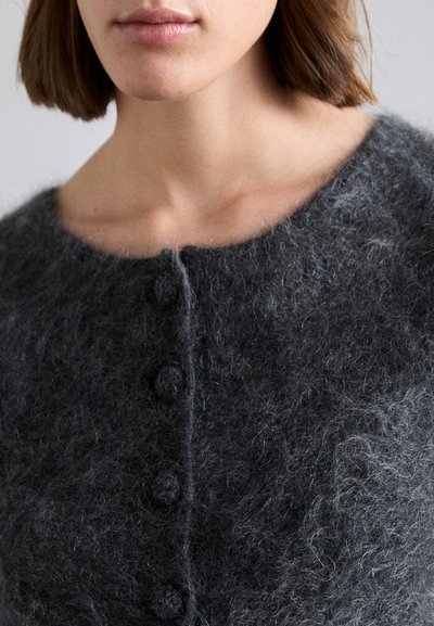 Cardigan grigio in lana con collo rotondo, caratterizzato da quattro bottoni testurizzati e una consistenza morbida e pelosa. La vista ravvicinata mostra i dettagli del tessuto.
