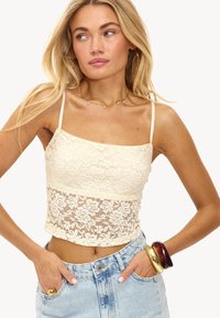 Kanten crop top in crème, met bloemenpatronen, dunne bandjes en een getailleerd ontwerp. Gecombineerd met hoge taille denim shorts.