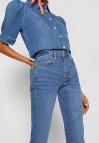 Conjunto de denim que presenta una camisa de botones de manga corta azul oscuro con mangas abullonadas y jeans de cintura alta, ambos en una tela suave.