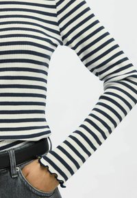 Gestreiftes navyblaues und weißes, ribbed langärmliges Oberteil mit taillierter Form und Rüschensaum. Kombiniert mit hoch geschnittenen grauen Jeans und einem schwarzen Gürtel.