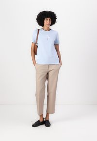 T-shirt en coton bleu clair à manches courtes, logo brodé sur la poitrine, associé à un pantalon cropped beige et des chaussures noires à enfiler.