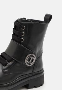 Svarte lær ankelstøvler med en robust såle, rund sølvdetalj med rhinestones, og tekstillisser. Glatt tekstur med en dekorativ stropp.