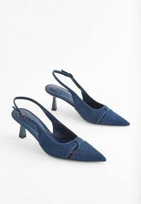 Denim slingback aukštakulniai su smailiu priekiu, turintys išpjovos dizainą ir kvadratinį kulną. Spalva yra sodriai mėlyna su tekstūruotu paviršiumi.