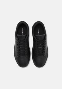 Baskets en cuir noir avec bout rond, semelle en caoutchouc plate, design à lacets et logo sur la languette, présentant un détail de couture minimaliste.