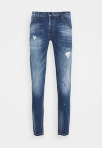 Jeans de mezclilla azul oscuro con un ajuste slim, que presentan áreas desgastadas, detalles de salpicaduras de pintura en verde y rojo, y un diseño clásico de cinco bolsillos.
