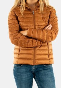 Veste matelassée marron avec couture horizontale, fermeture éclair à l'avant, col montant et poignets élastiques, associée à un jean bleu.