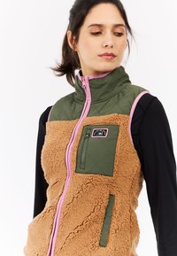 Bruine fleecvest met een olijfgroen gewatteerd bovenstuk en roze accenten. Voorzien van een ritssluiting borstzak en een hoge kraag.