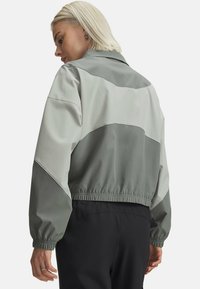 Šedá a světle šedá bunda s blokovým barevným designem, límcem, elastickými manžetami a stahováním v pase. Hladká, lehká tkanina.