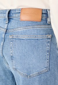 Lichtblauwe denim jeans met een leren label "Marc O'Polo." Beschikt over klassieke achterzakken en verstevigde stikseldetails.