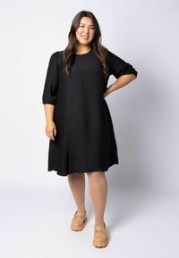 Schwarzes, strukturiertes Kleid mit drei Viertel Puffärmeln und A-Linien-Silhouette. Kombiniert mit hellbraunen, klobigen Loafers.
