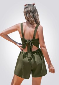 Mono verde oliva con tirantes gruesos, diseño de espalda atada y cintura elástica. Tejido texturizado, pantalones cortos holgados y detalle de espalda descubierta.