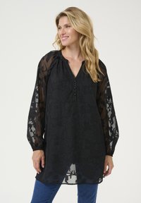 Black tunic with sheer long sleeves, floral pattern, V-neck, and button detailing. Relaxed fit with textured fabric and gathered accents.