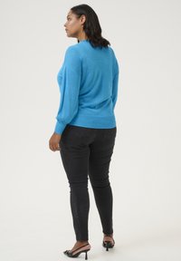 Lichtblauwe pullover van een zachte, rekbare stof met lange pofmouwen, gecombineerd met zwarte skinny jeans en zwarte sandalen met hak.