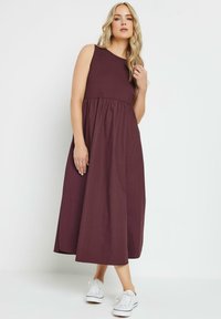 Vestido largo sin mangas de color burdeos con cintura fruncida, escote redondo y falda fluida, combinado con zapatillas blancas. Tela de algodón suave.
