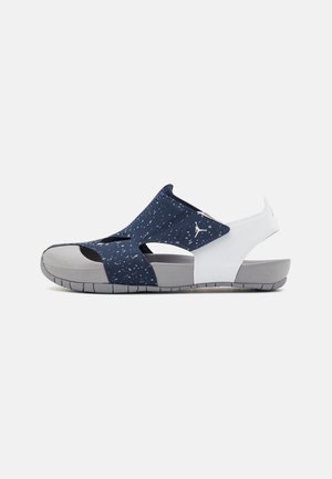 Sandal fermé à l'avant avec une tige bleu marine à pois, une sangle blanche au talon, une semelle grise et le logo Air Jordan sur le côté.