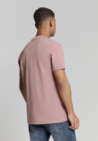 Polo shirt in lichtroze stof met korte mouwen en een kraag, voorzien van een gladde textuur en subtiele stikdetails op de achterkant.