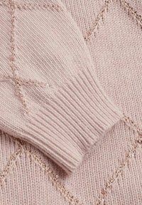 Lichtroze gebreide trui mouw met geribbelde manchetten en diagonale glanzende draadaccenten die een subtiel diamantpatroon vormen.