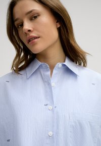 Gestreiftes Hemd in Hellblau und Weiß, mit Kragen, weißen Knöpfen und Logo-Akzenten auf dem Stoff. Slim-Fit-Design.