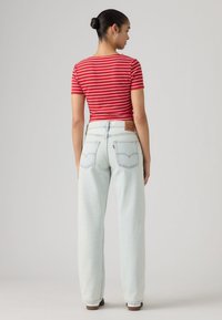 Κοντομάνικο τοπ με κόκκινες και λευκές ρίγες, συνδυασμένο με ανοιχτό μπλε τζιν ψηλόμεσο, με δερμάτινη ετικέτα και τέσσερις πίσω τσέπες.