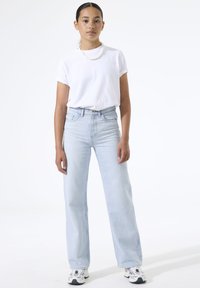 Camiseta blanca de manga corta combinada con vaqueros de pierna ancha de talle alto en azul claro y zapatillas blancas, con un brillo sutil y un diseño clásico.